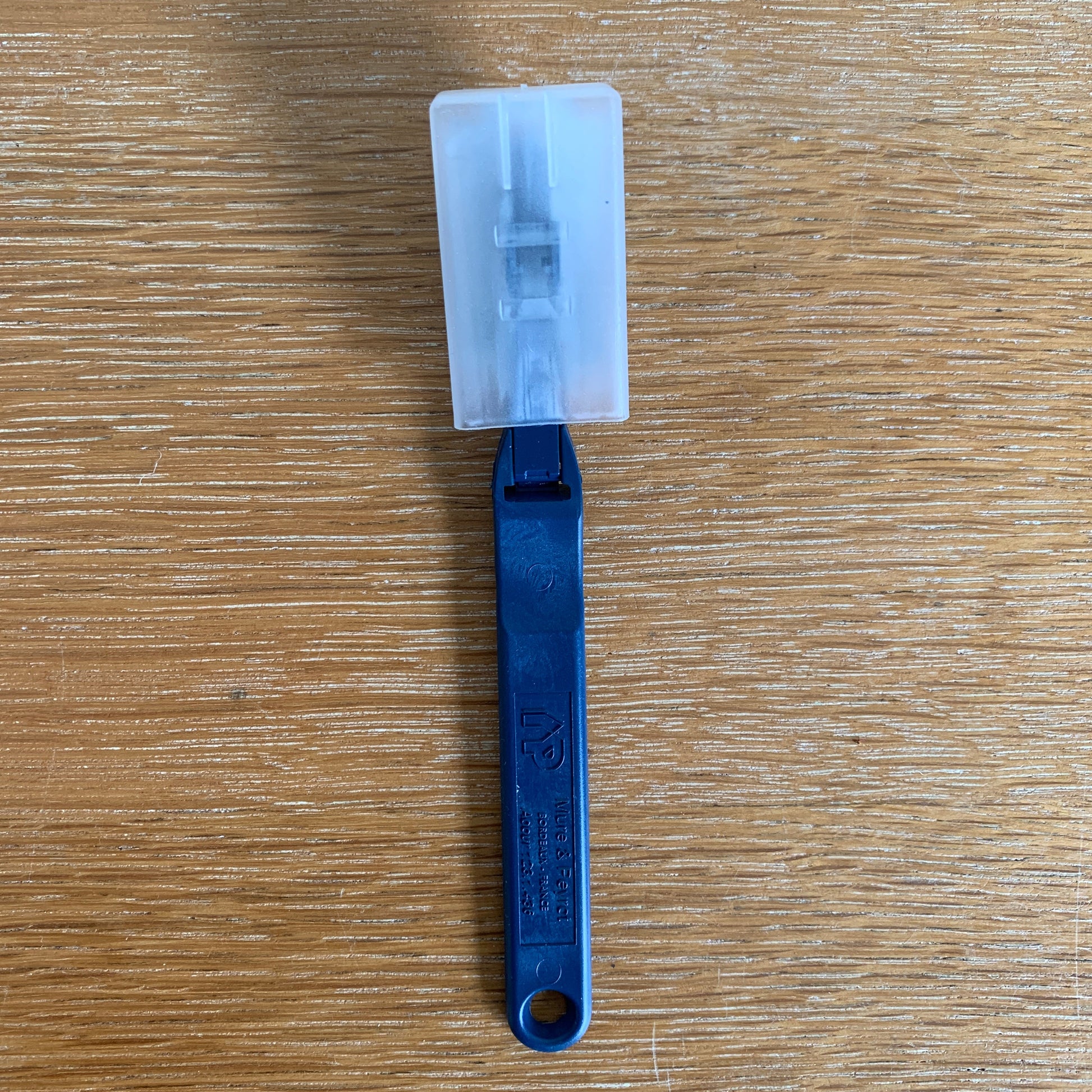 Blue plastic tool with a white rectangular component on a wooden surface